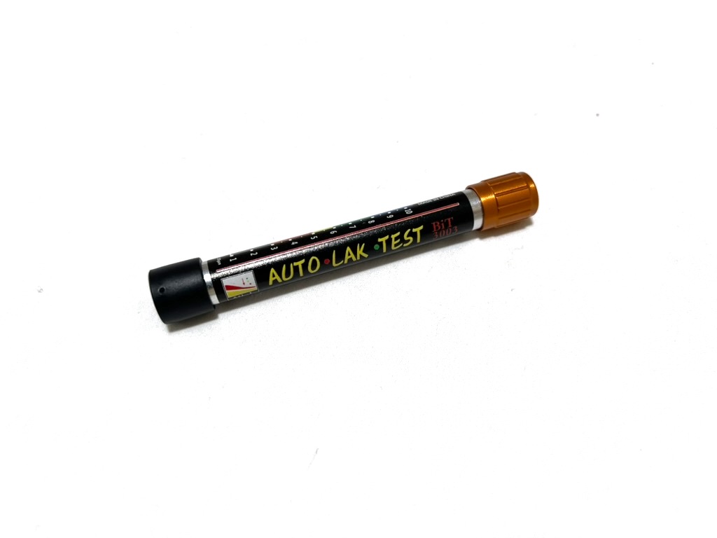 The paint thickness gauge from the kit, a pen-sized tube with a black end cap, an orange cap and a printed thickness scale